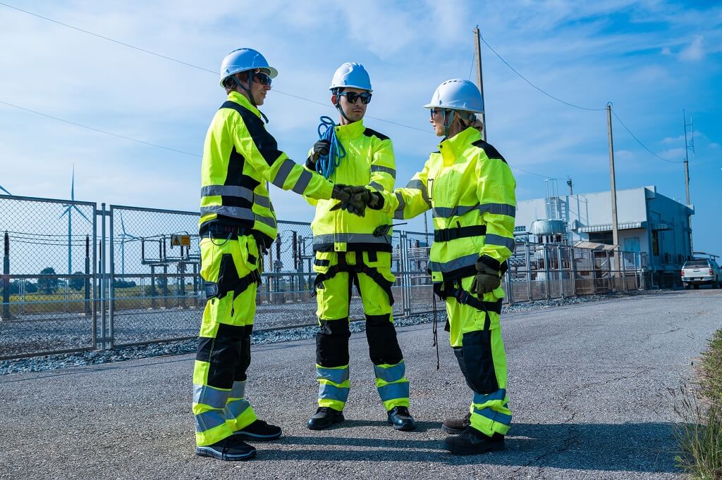 Tri radnika u zaštitnoj opremi razgovaraju na industrijskoj lokaciji