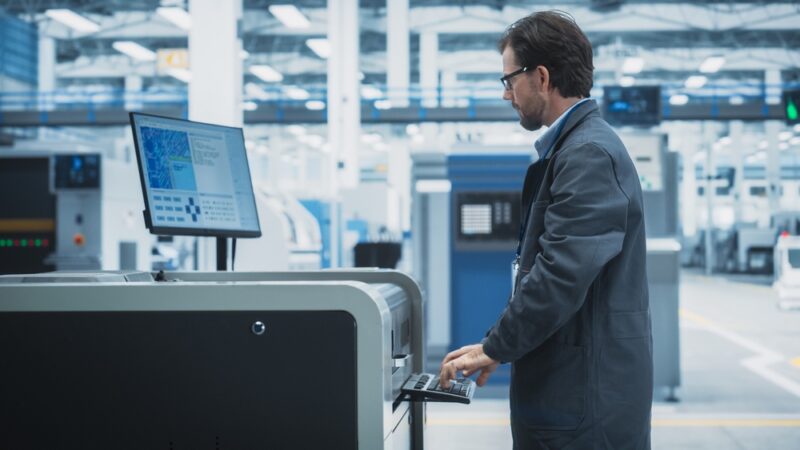 Inženjer upravlja industrijskim sistemom preko računara u modernoj fabrici, prateći podatke u realnom vremenu