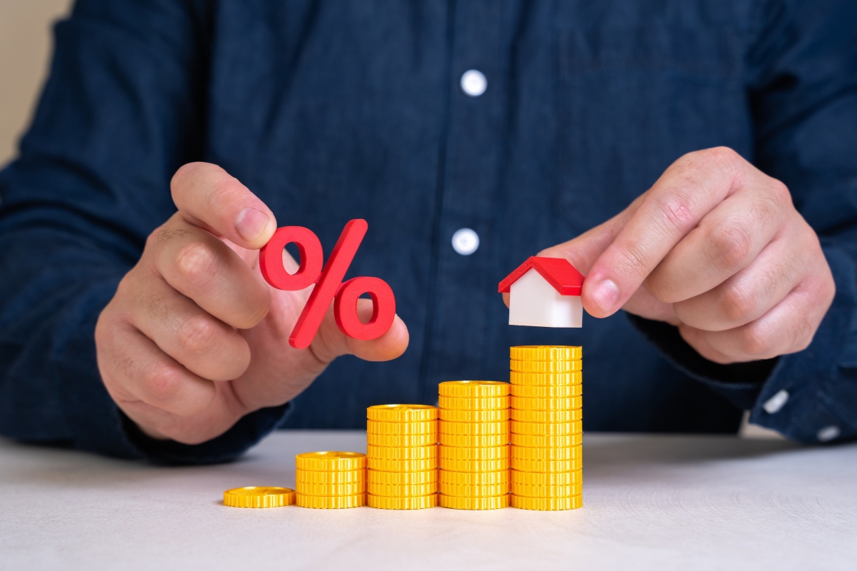 prikaz osobe koja drži u ruci kućicu i kamatnu stopu i novac ispod