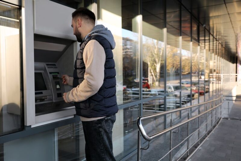 Muškarac podiže novac na bankomatu ispred poslovnice banke u urbanom okruženju