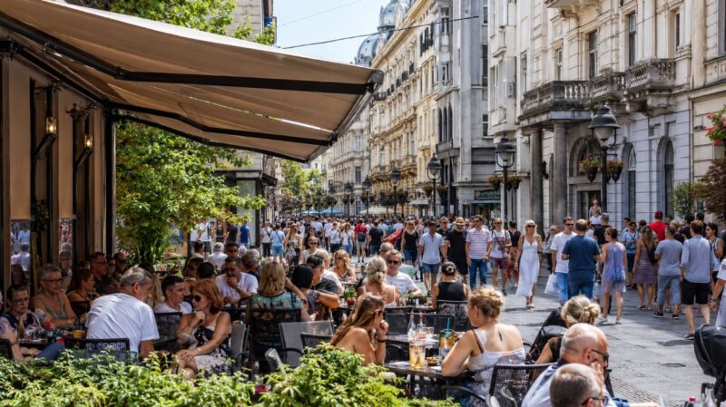 Puna bašta kafića u centru Beograda sa turistima tokom prolećnog ili jesenjeg dana.
